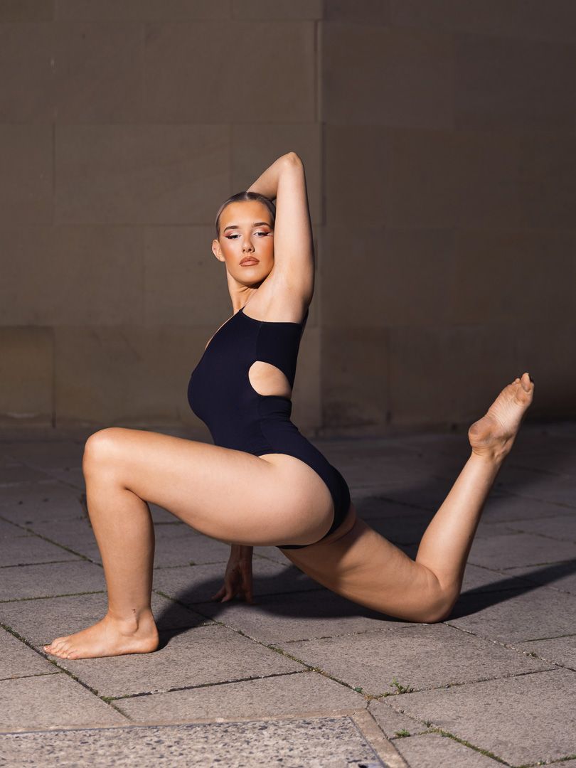 Dancer performs contemporary floor movements in a black leotard against concrete background.
