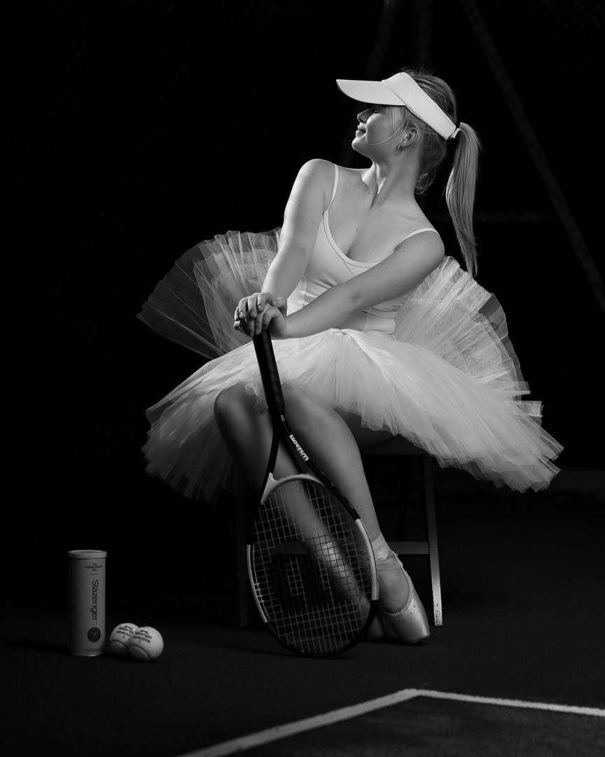 Black and white portrait of ballerina in tutu posing with tennis racket.