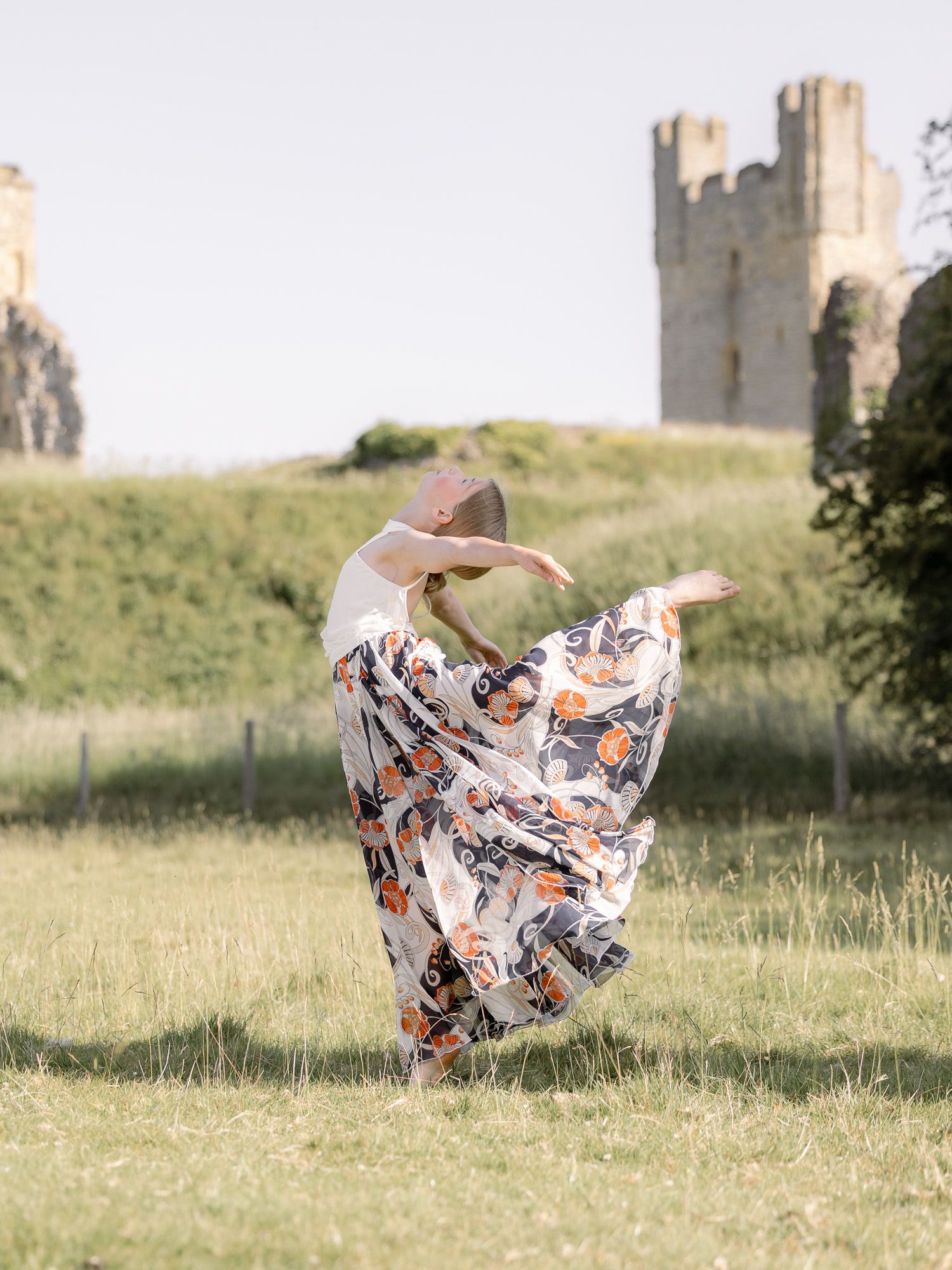 Flowing dress creates artistic motion blur as dancer spins in grassy field near castle.