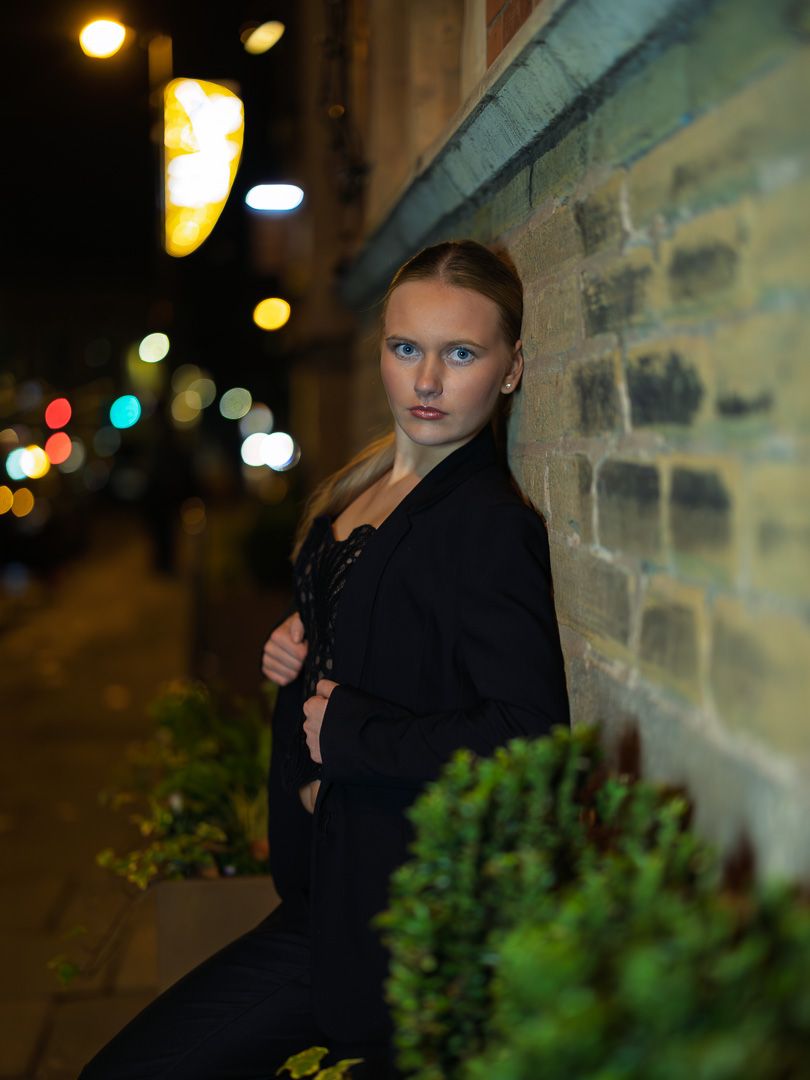 A moody nighttime fashion shoot in an urban alley with brick walls and ambient lighting.