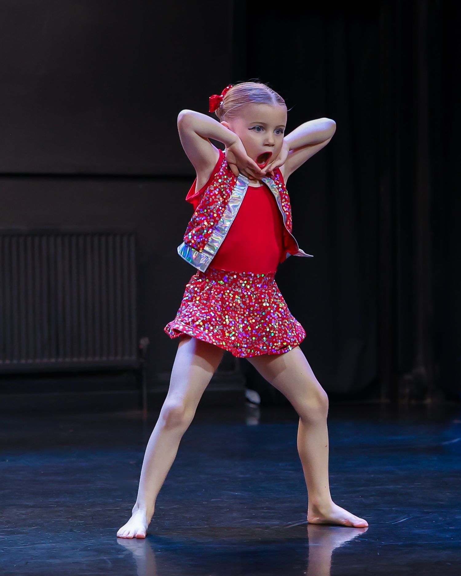 Young girl in red dance costume performs energetic routine on stage.