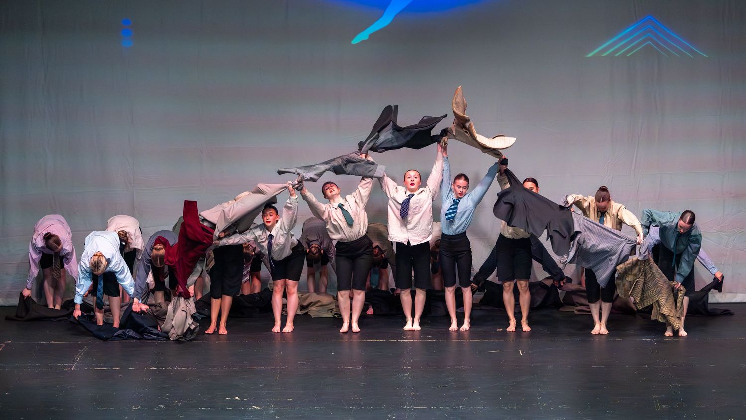 Group of dancers performing on stage with flowing fabric costumes under blue stage lighting.