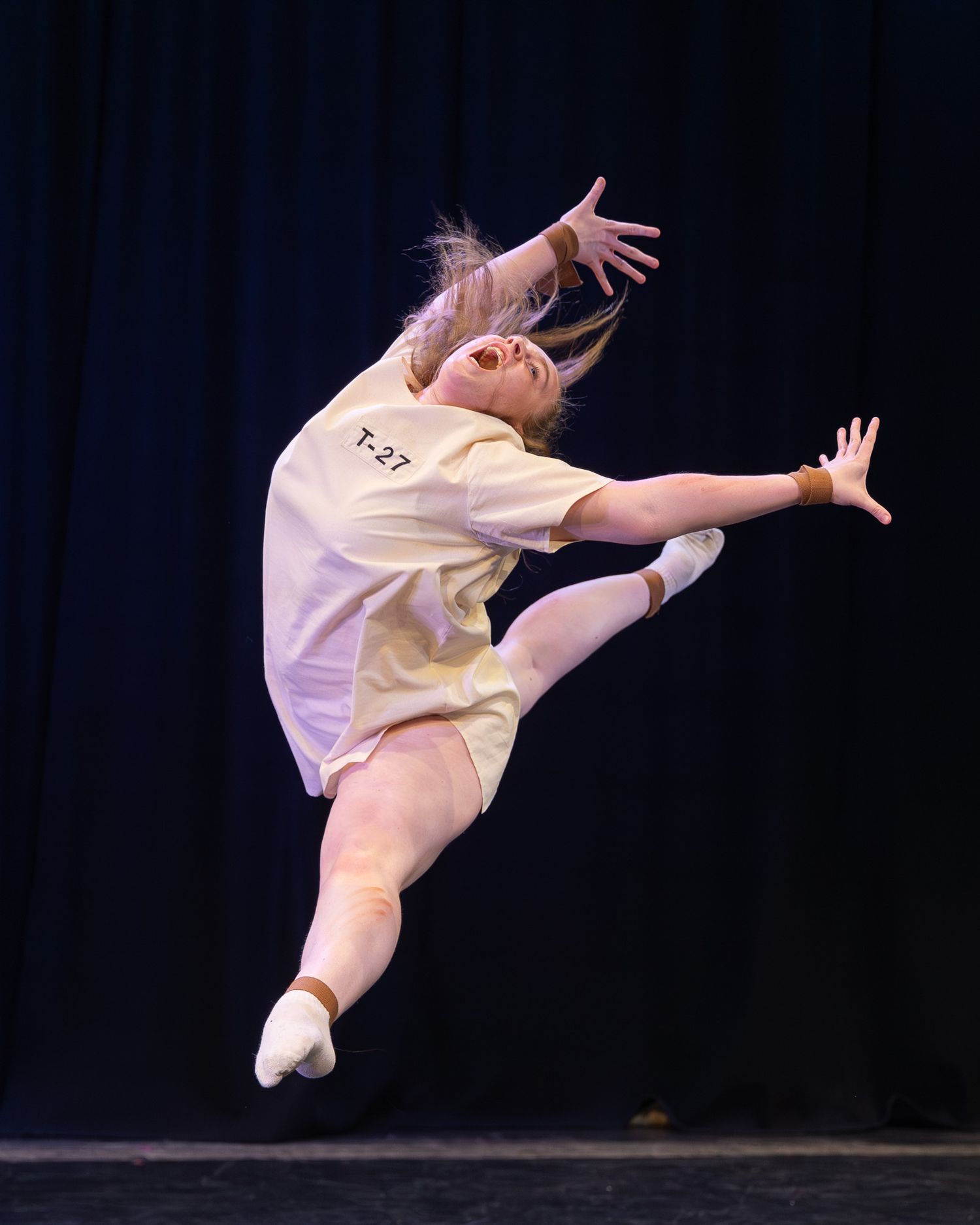 Young dancer in yellow outfit leaping gracefully on stage during a ballet performance competition.