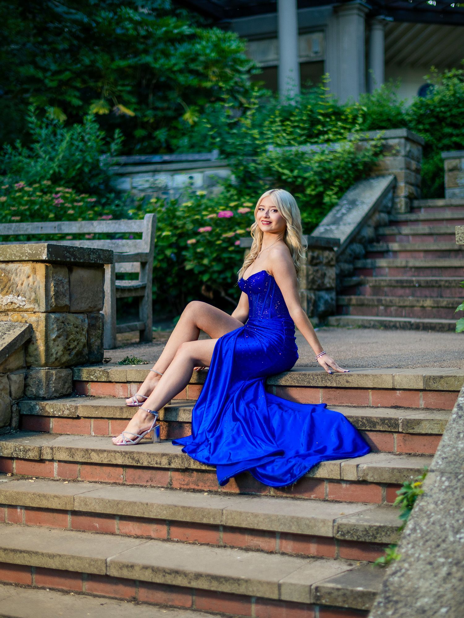 A blonde woman poses gracefully on stone steps in a stunning royal blue strapless gown with a flowing train.