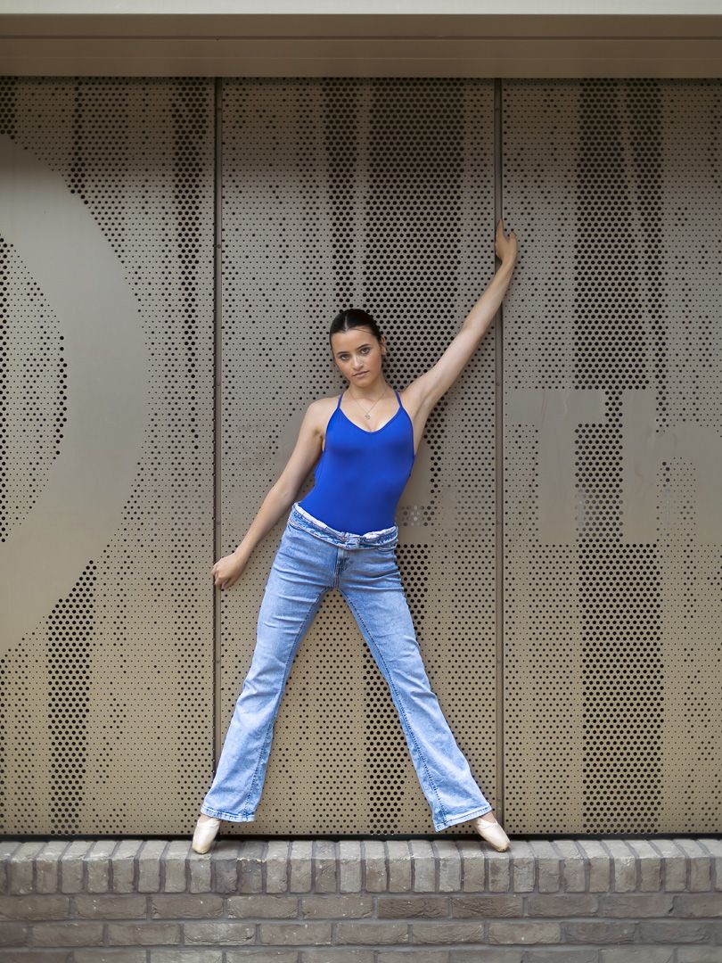 Young woman in blue tank top and jeans posing gracefully against a perforated metal wall outdoors.