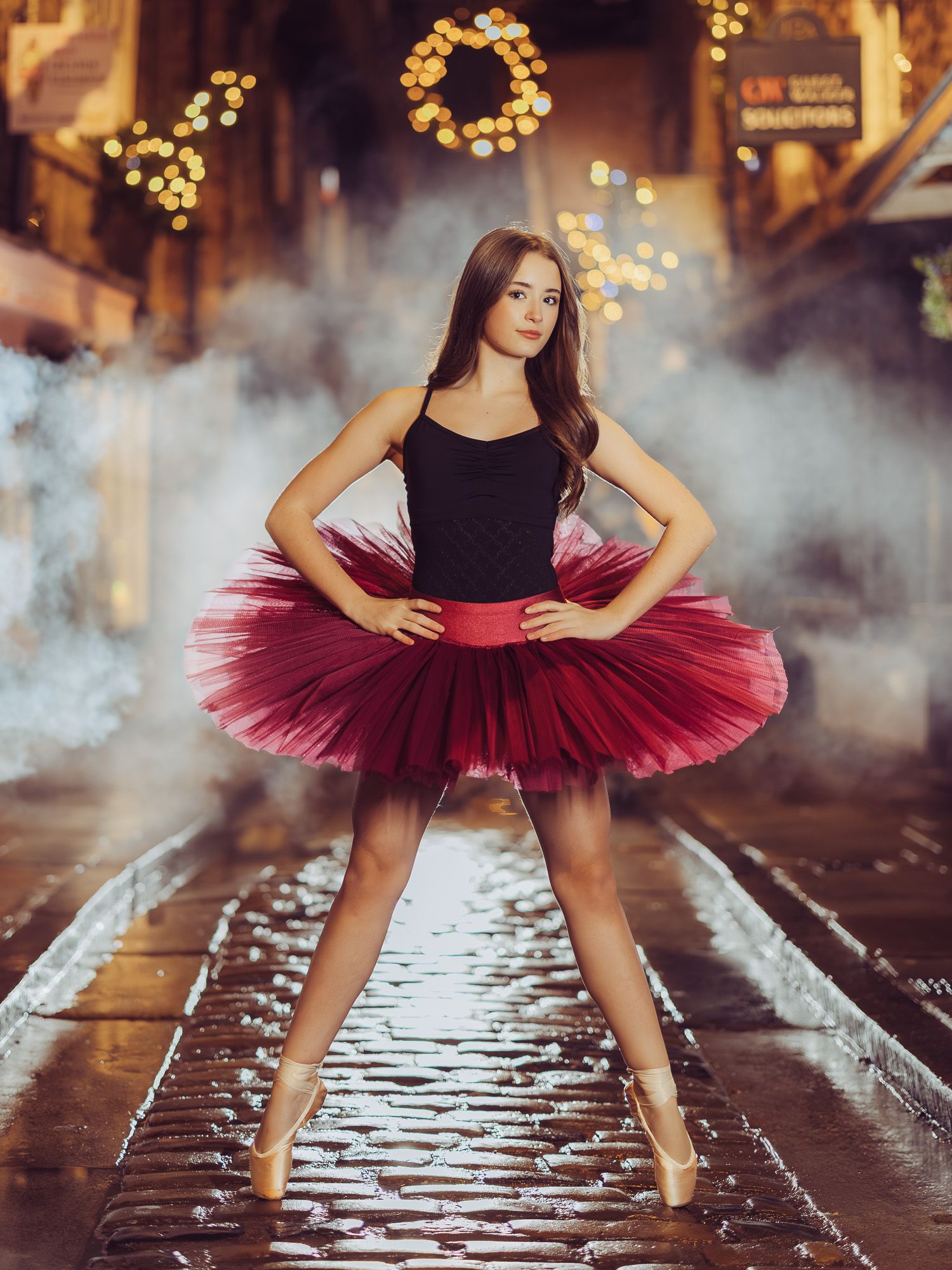 A ballerina in a red tutu performs graceful poses on wet cobblestones with atmospheric fog and twinkling lights.
