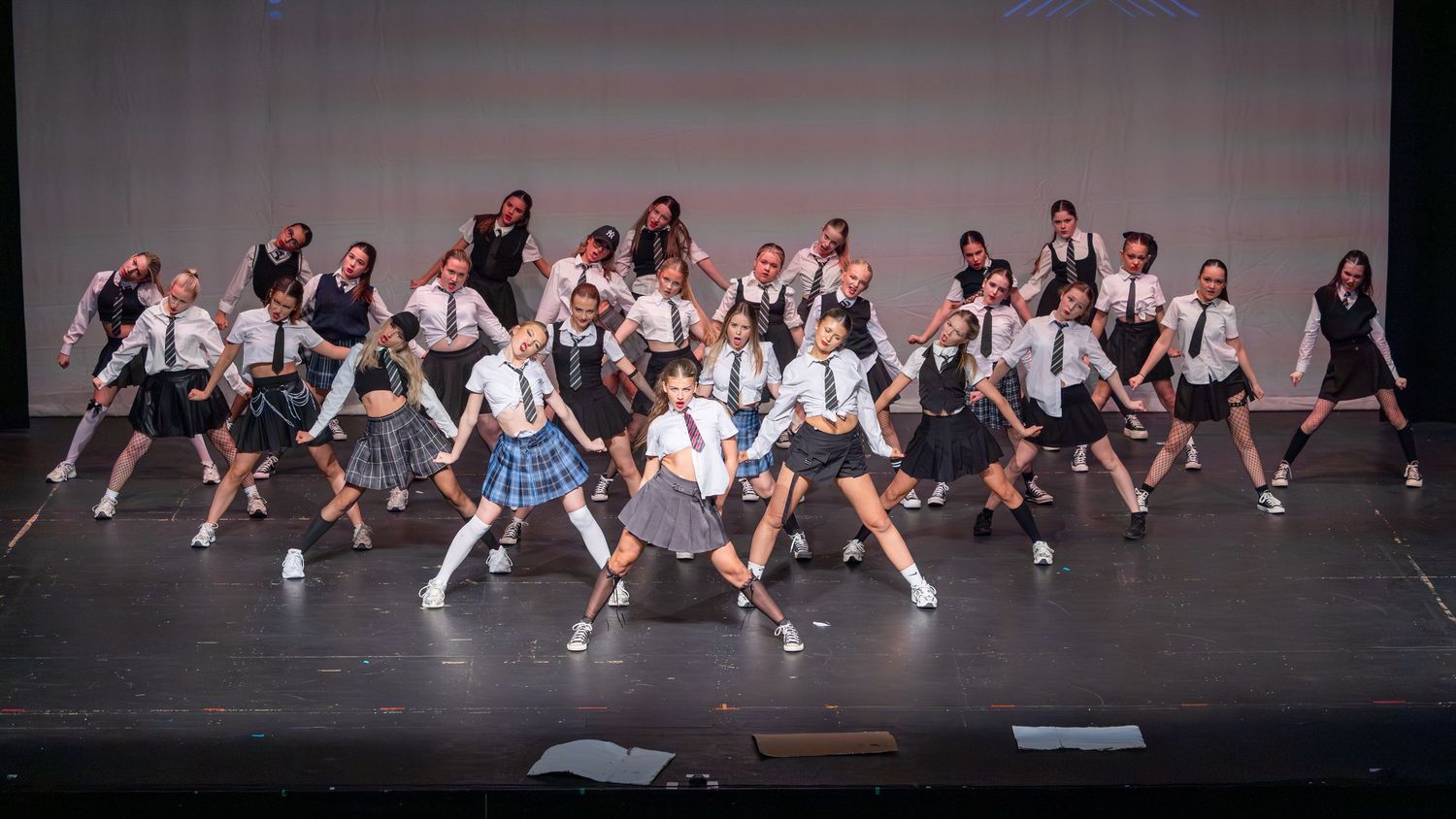 Students in school uniforms perform a choreographed dance routine on a theater stage during a group performance.