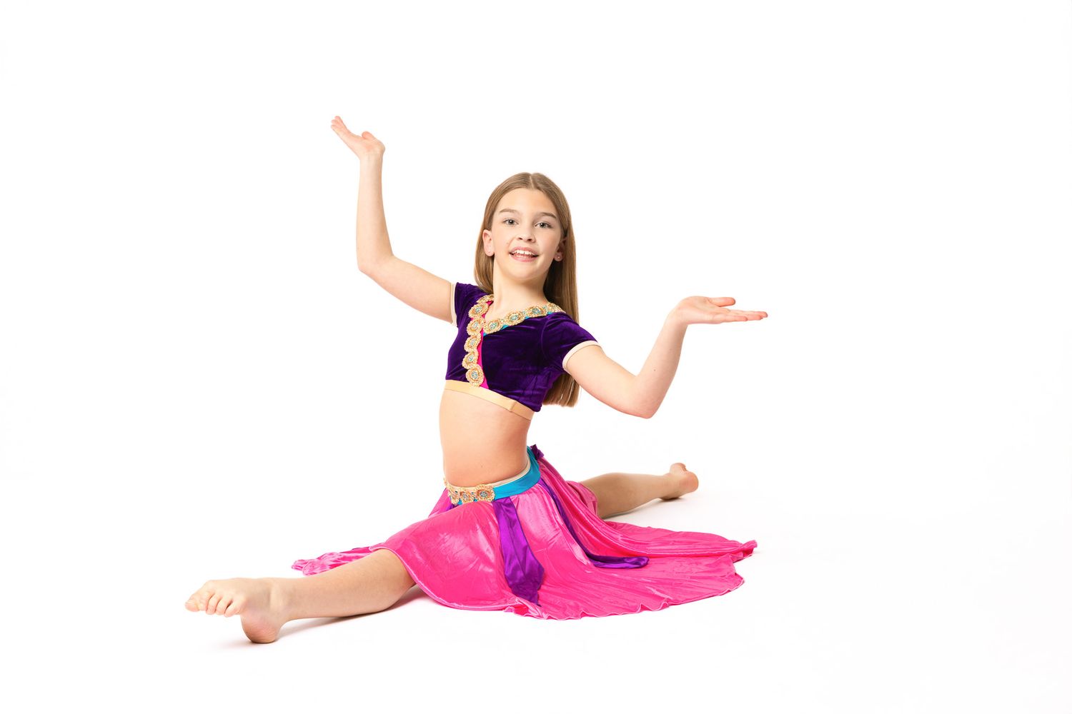 Dancer in pink leotard performs graceful split leap with arms outstretched against white background.