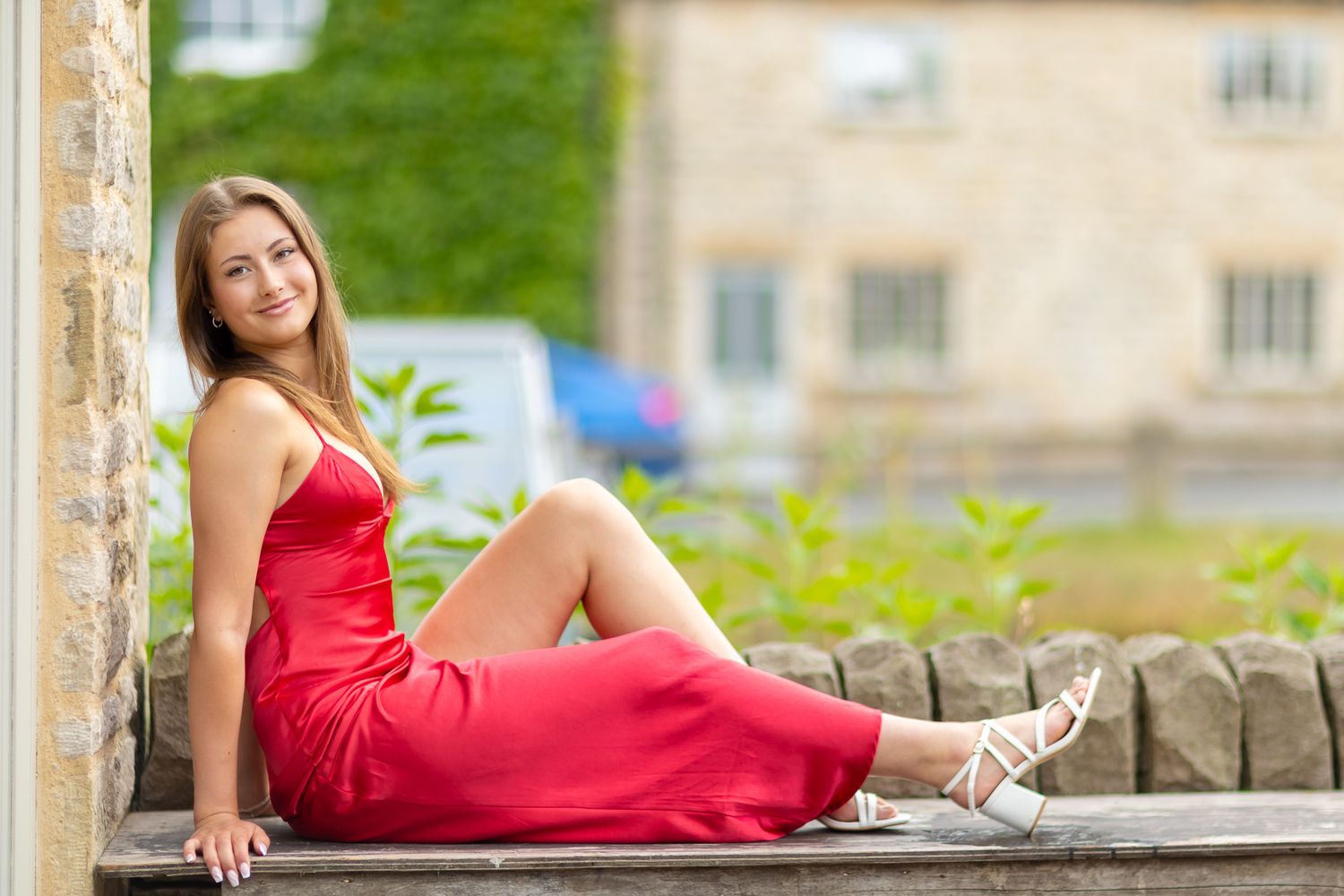 Someone in a red dress poses on a stone wall with historic architecture in the background.