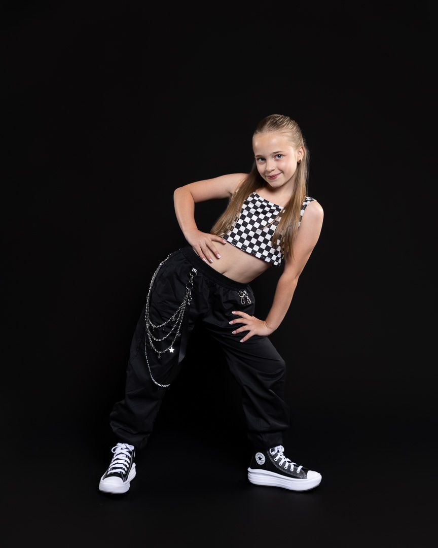Young girl in checkered crop top and black cargo pants strikes a hip-hop dance pose in studio.