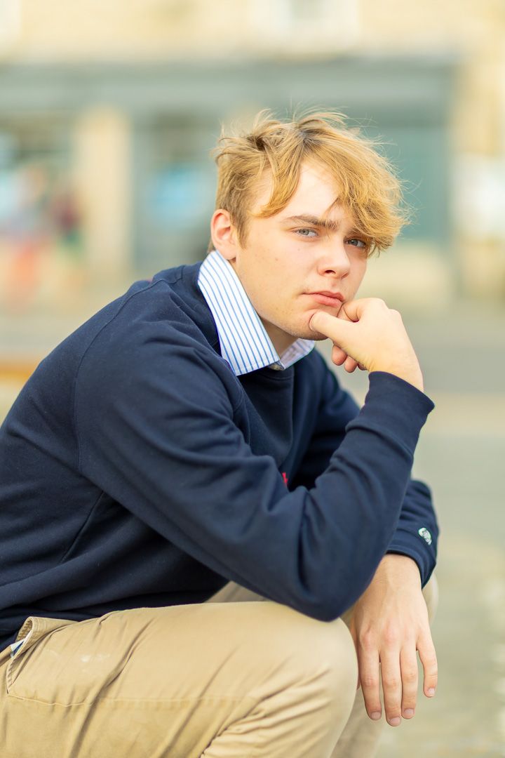 Person in navy sweater and khaki pants reclines thoughtfully against blurred outdoor background.