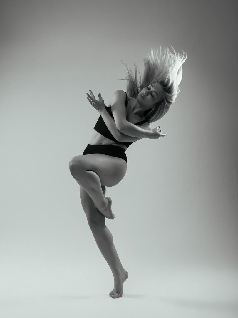 Black and white photo of a female dancer mid-movement with hair flowing, wearing a black sports bra and shorts.