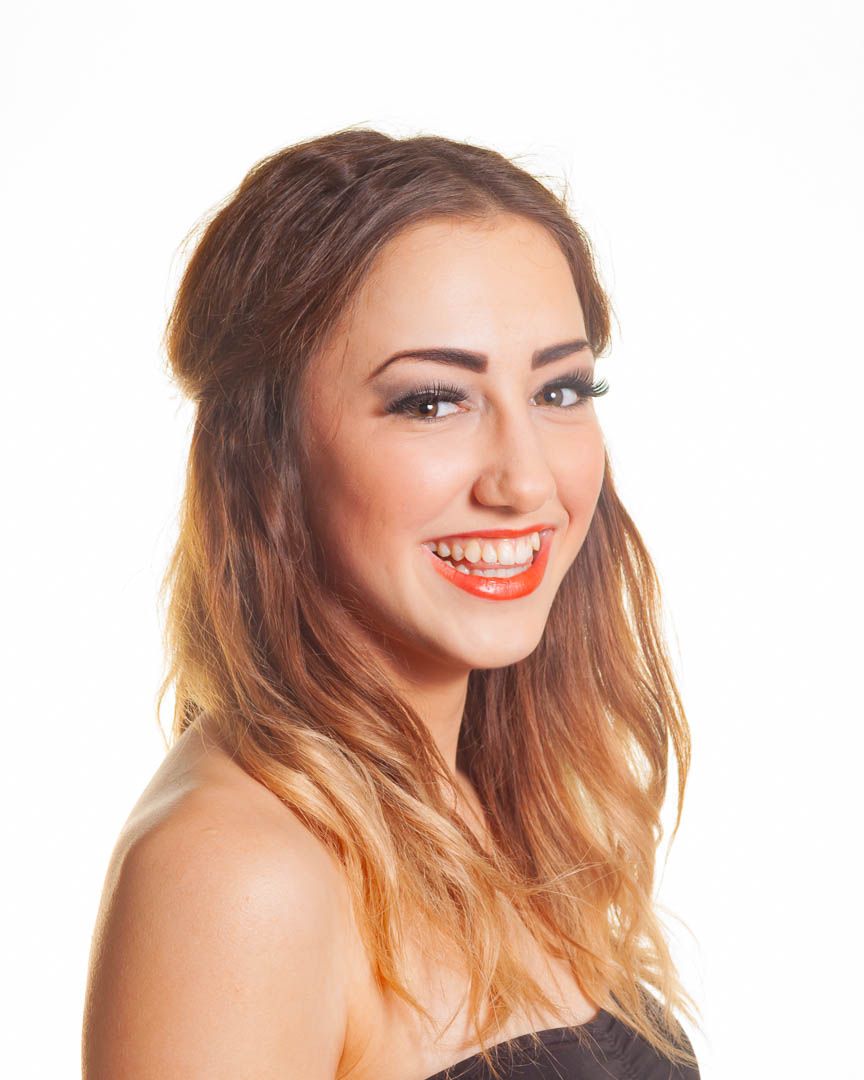 Smiling young woman with long brown ombre hair, red lipstick, and strapless top against white background.