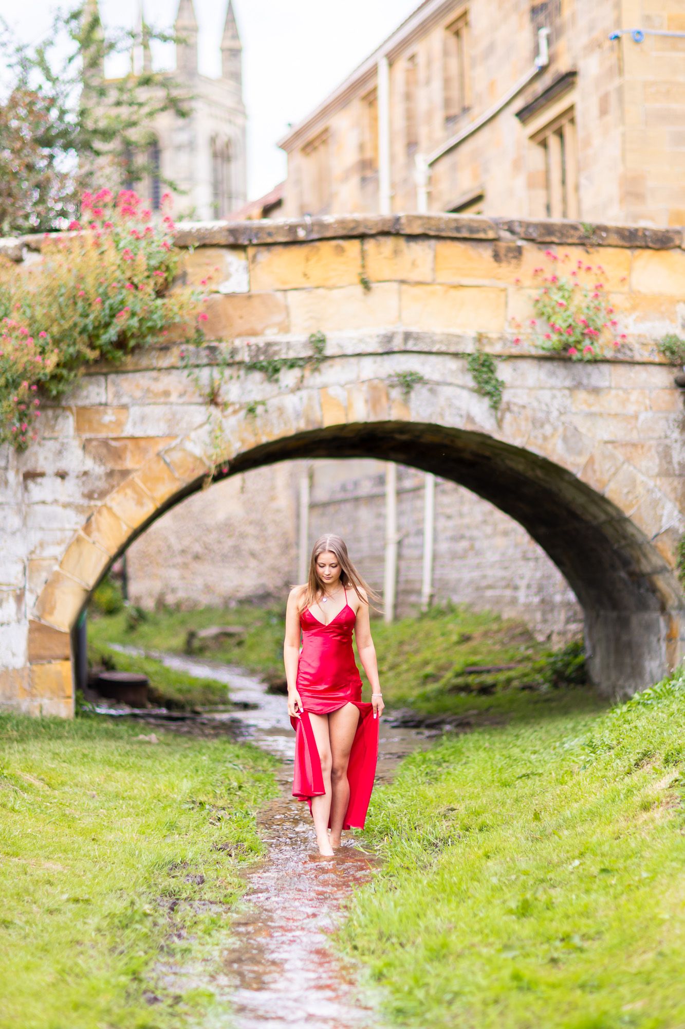 Artistic outdoor photo series near a stone bridge with flowing water and someone in a red dress.