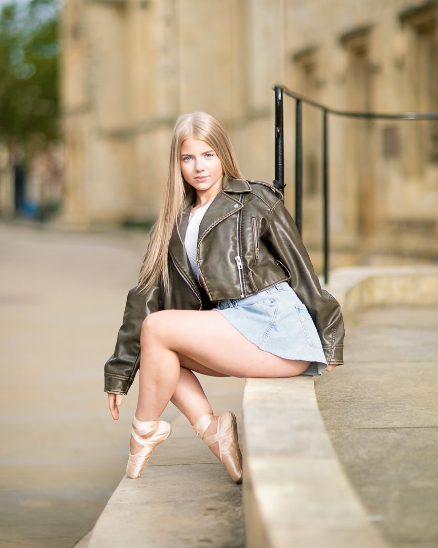 Ballet dancer in leather jacket strikes urban poses against stone architecture.