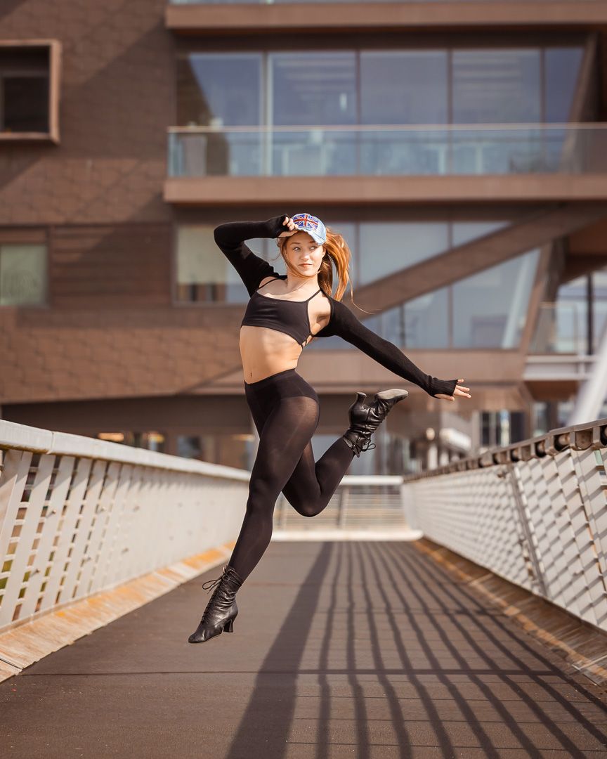 Athletic dancer leaps gracefully on urban walkway wearing black activewear.