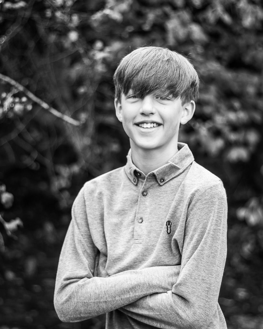 Black and white portrait of a young person in a collared shirt smiling outdoors.