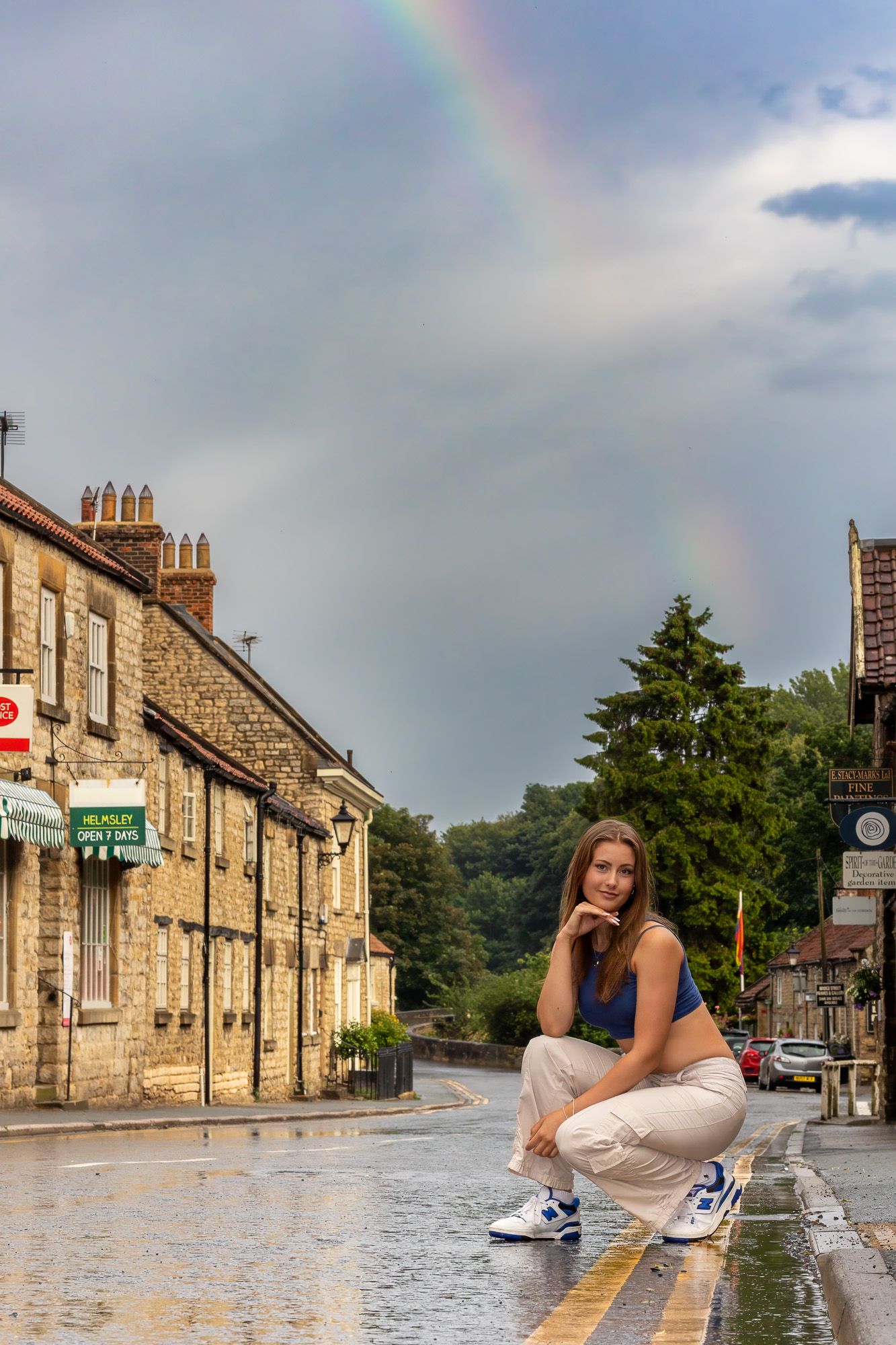 A casual street photo with a rainbow in the background on a wet cobblestone street.