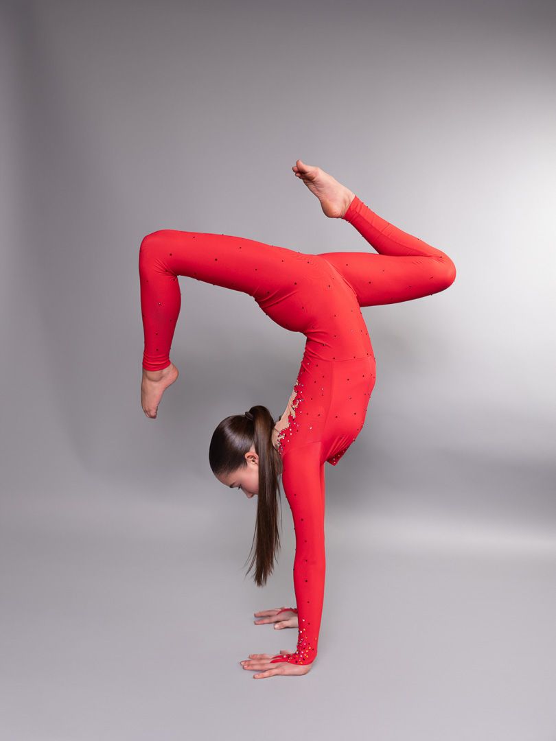 Gymnast in red bodysuit demonstrates advanced flexibility poses in sequence against grey background.