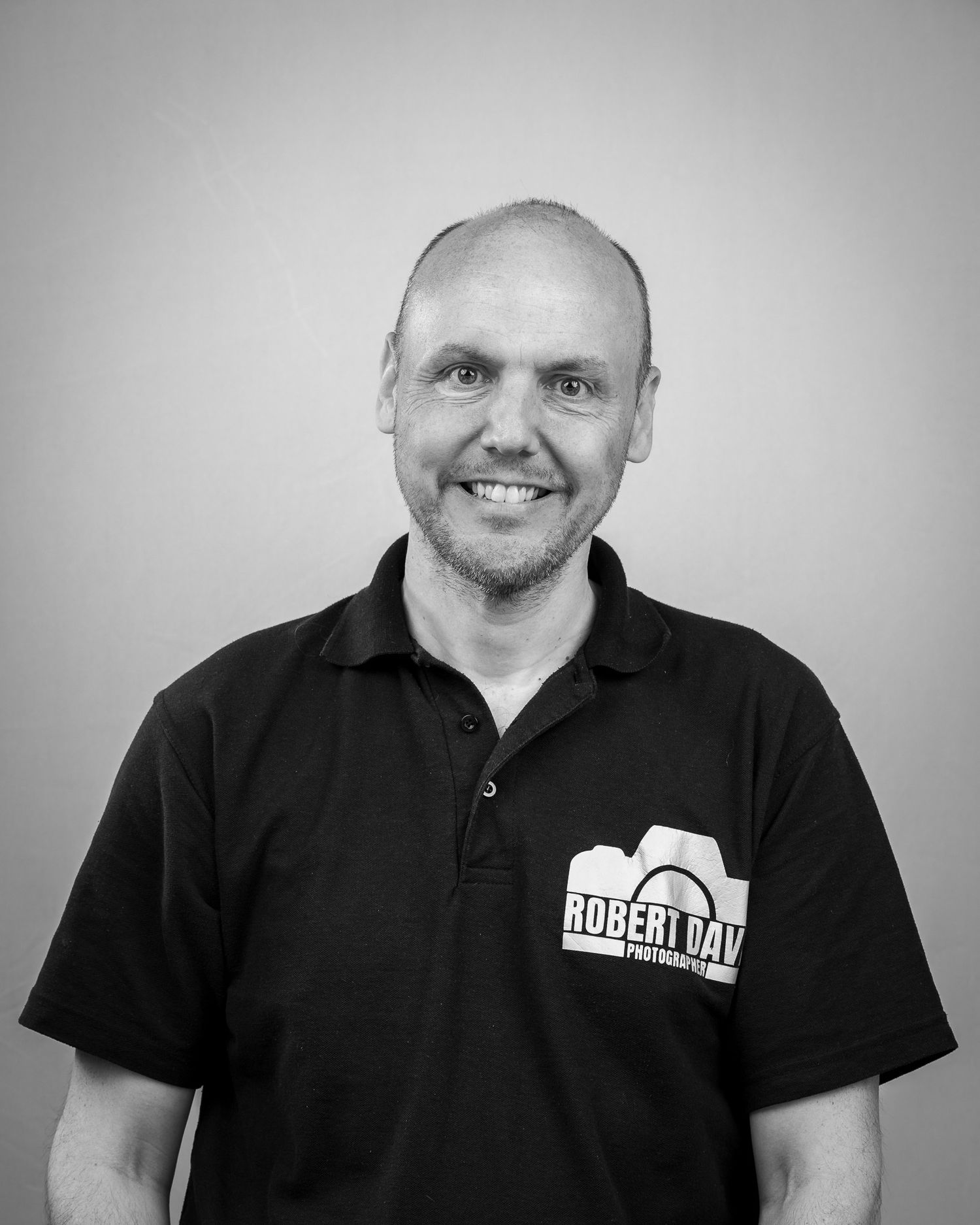 Professional headshot of person wearing black polo shirt with company logo.