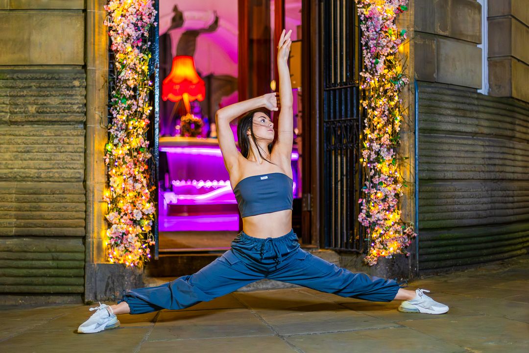 Dancer strikes athletic pose in front of colorful holiday window display.