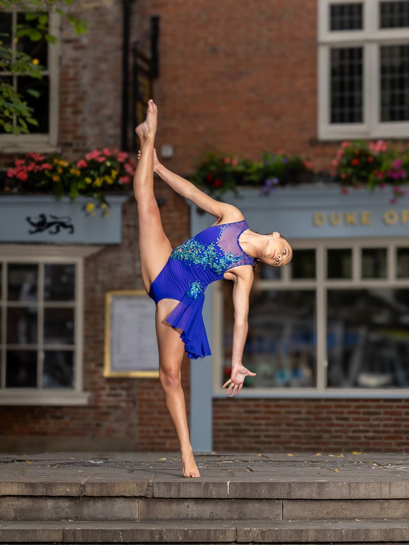 Athletic dance poses performed on an outdoor ledge against brick building backdrop.