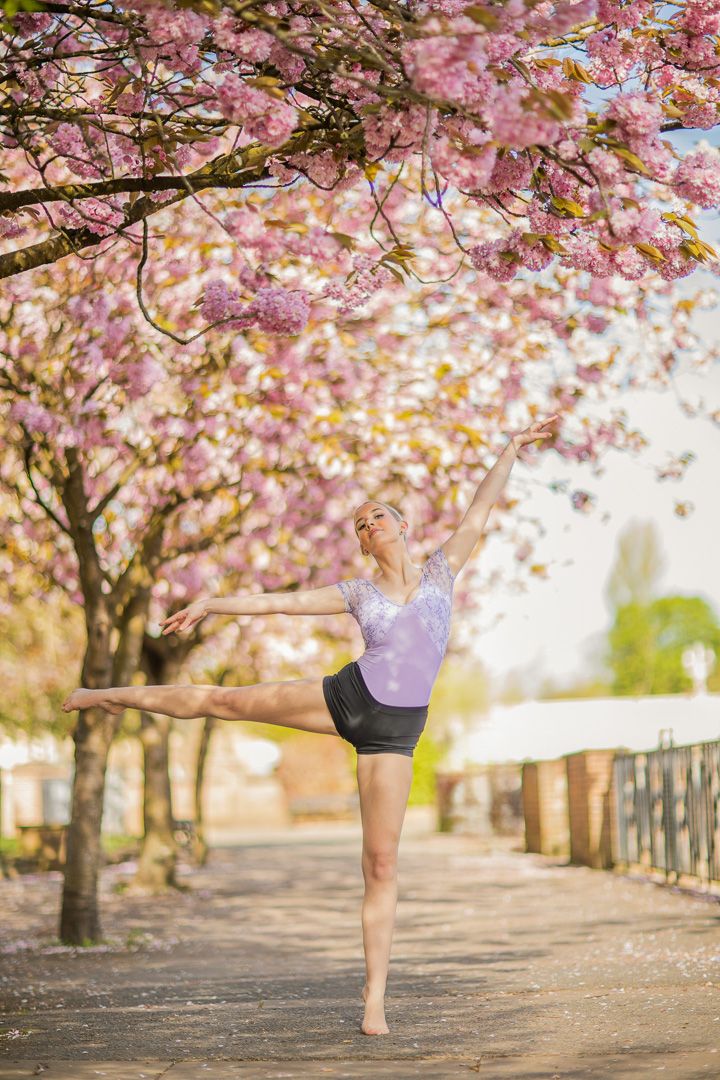 Dancer performs elegant movements under blooming cherry blossom trees.