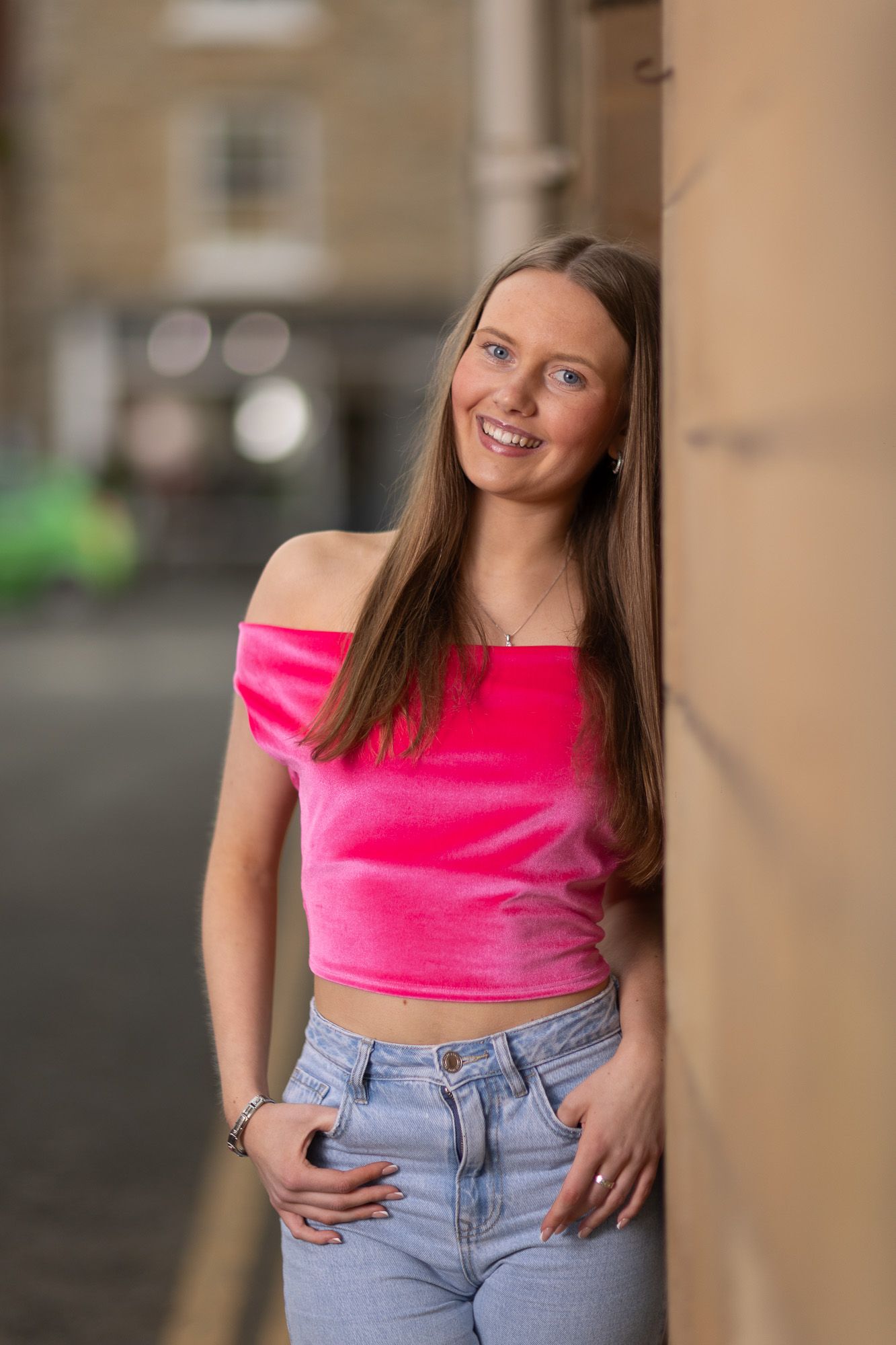 Urban fashion portrait with pink crop top and denim jeans against neutral background.