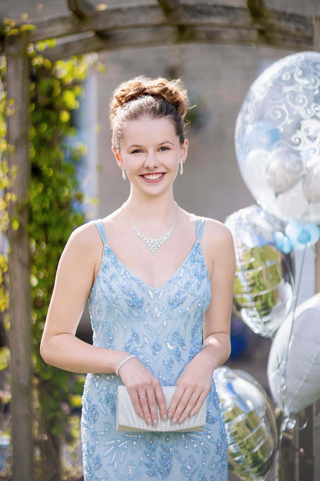 A formal portrait with silver balloons showing someone in a light blue beaded gown and necklace.