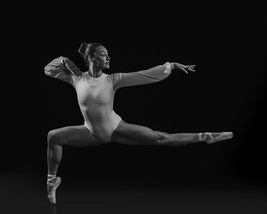 Black and white photo of a ballet dancer mid-leap in a powerful grand jete wearing pointe shoes.