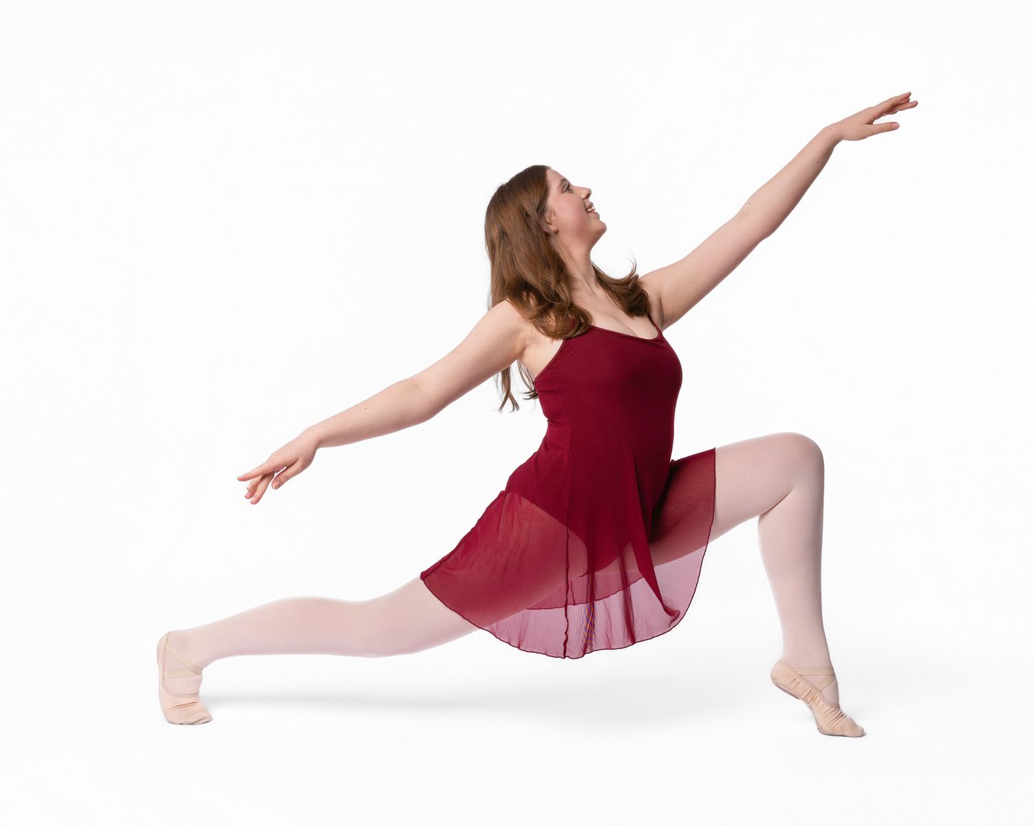 A dancer in a flowing burgundy dress performs a graceful lunge position with outstretched arms against a white background.