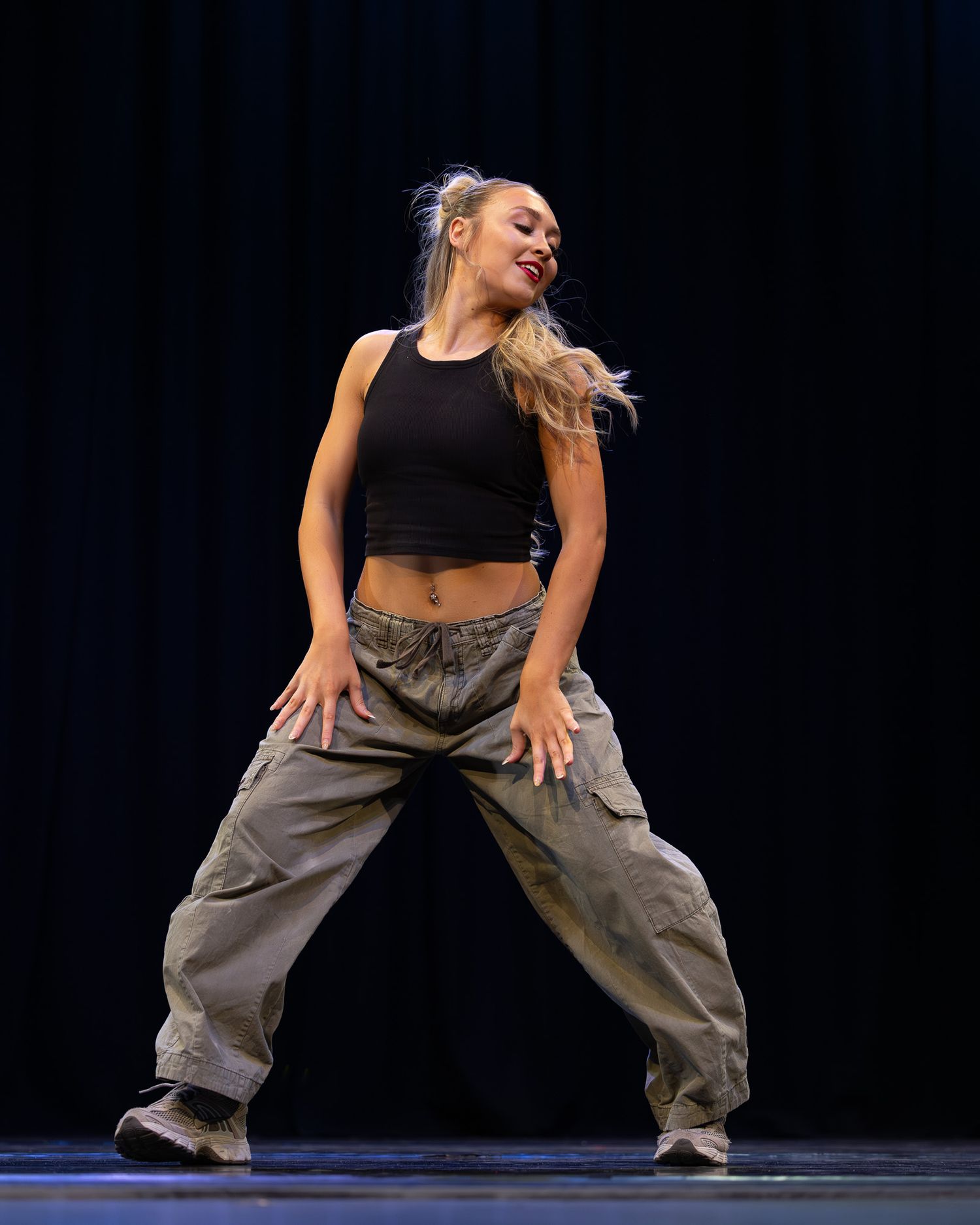 Female dancer performing hip-hop routine on stage wearing black crop top and baggy cargo pants.