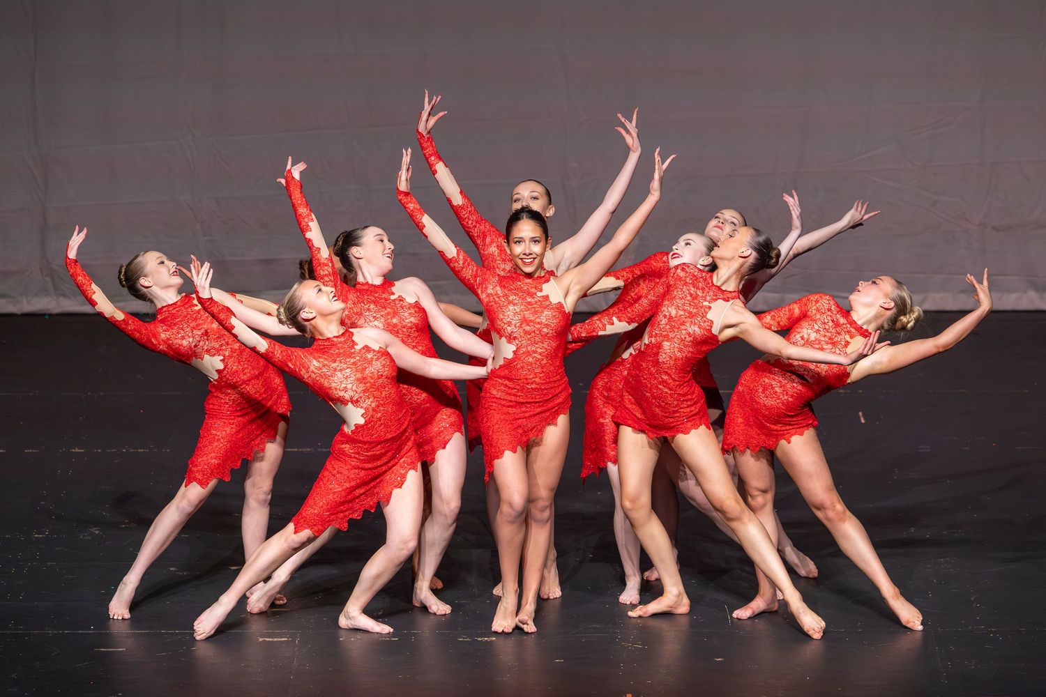 Group of dancers in red lace costumes performing a synchronized routine on a dark stage.