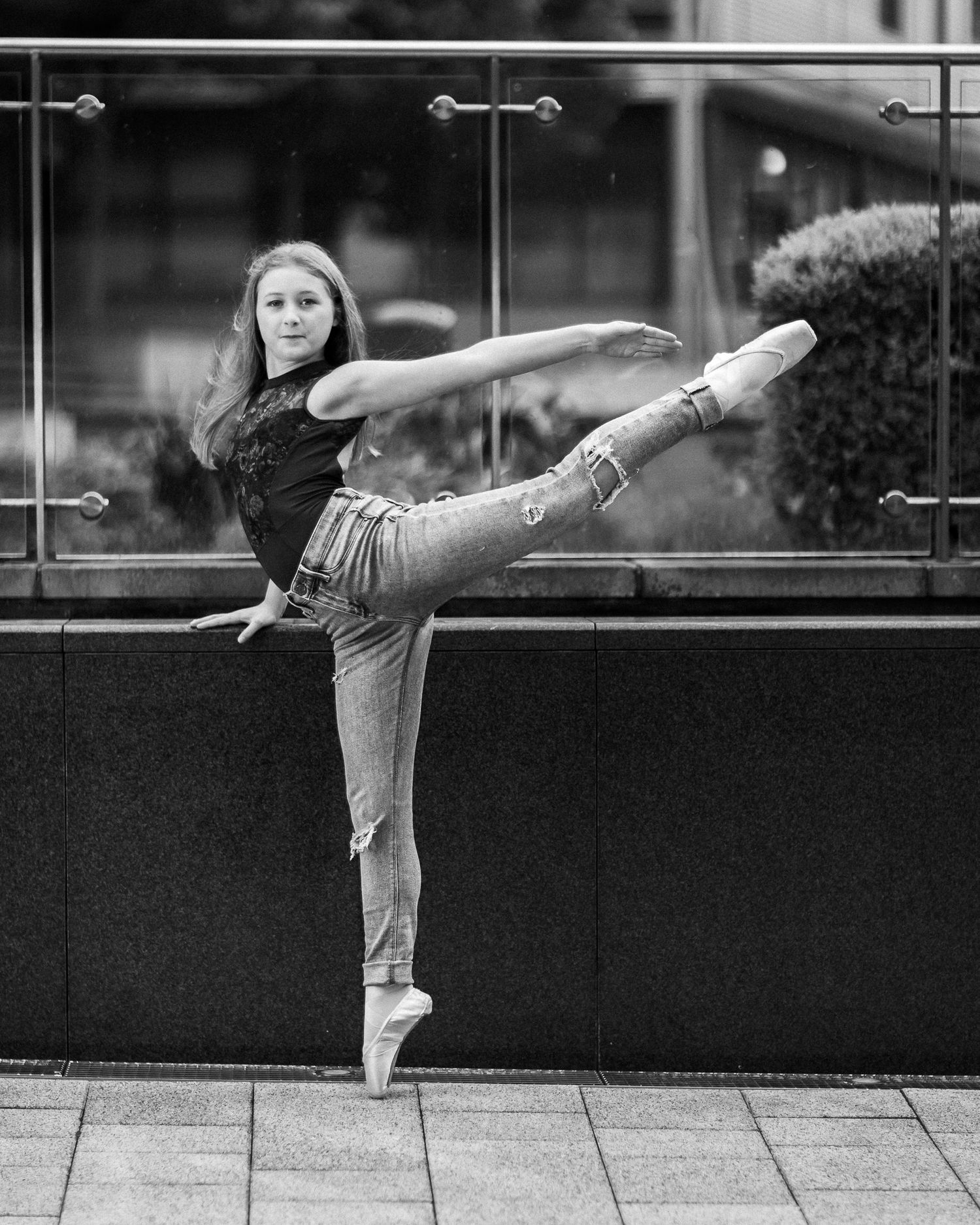 A dancer performs a graceful arabesque pose in black and white against an urban backdrop.