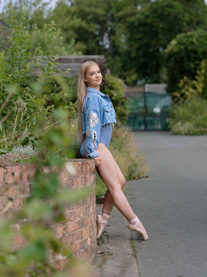 Ballet dancer in casual denim performs elegant poses along brick wall pathway.