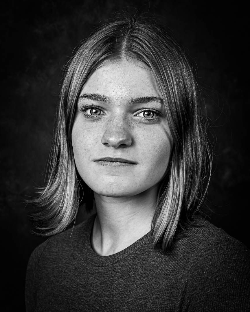 Black and white portrait of a young woman with shoulder-length hair and freckles, studio photography.