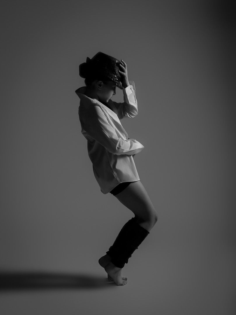 Black and white photo of a dancer in dramatic pose wearing oversized shirt and leg warmers.