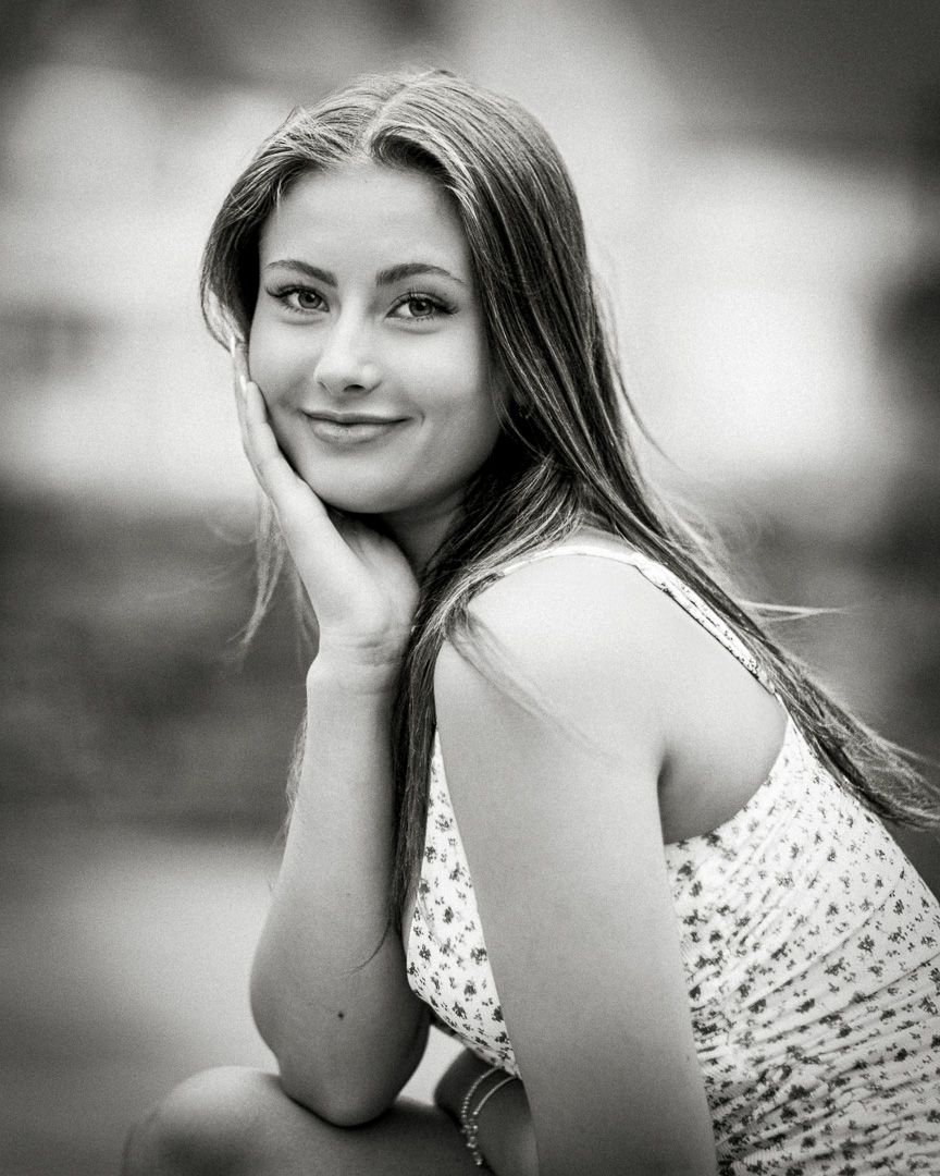 A black and white portrait of a young woman in a polka dot top resting her hand on her cheek.