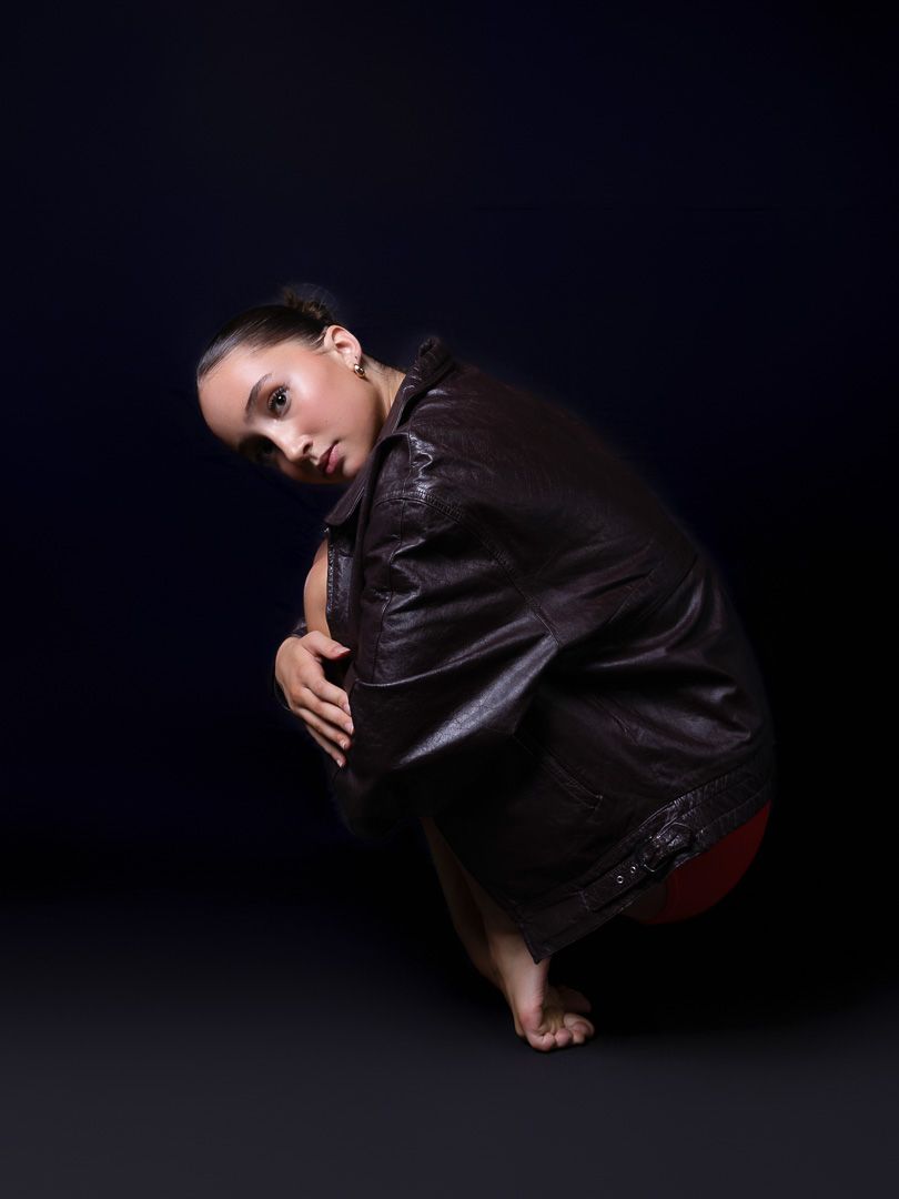 Figure in dark clothing performs expressive contemporary dance movement on floor.