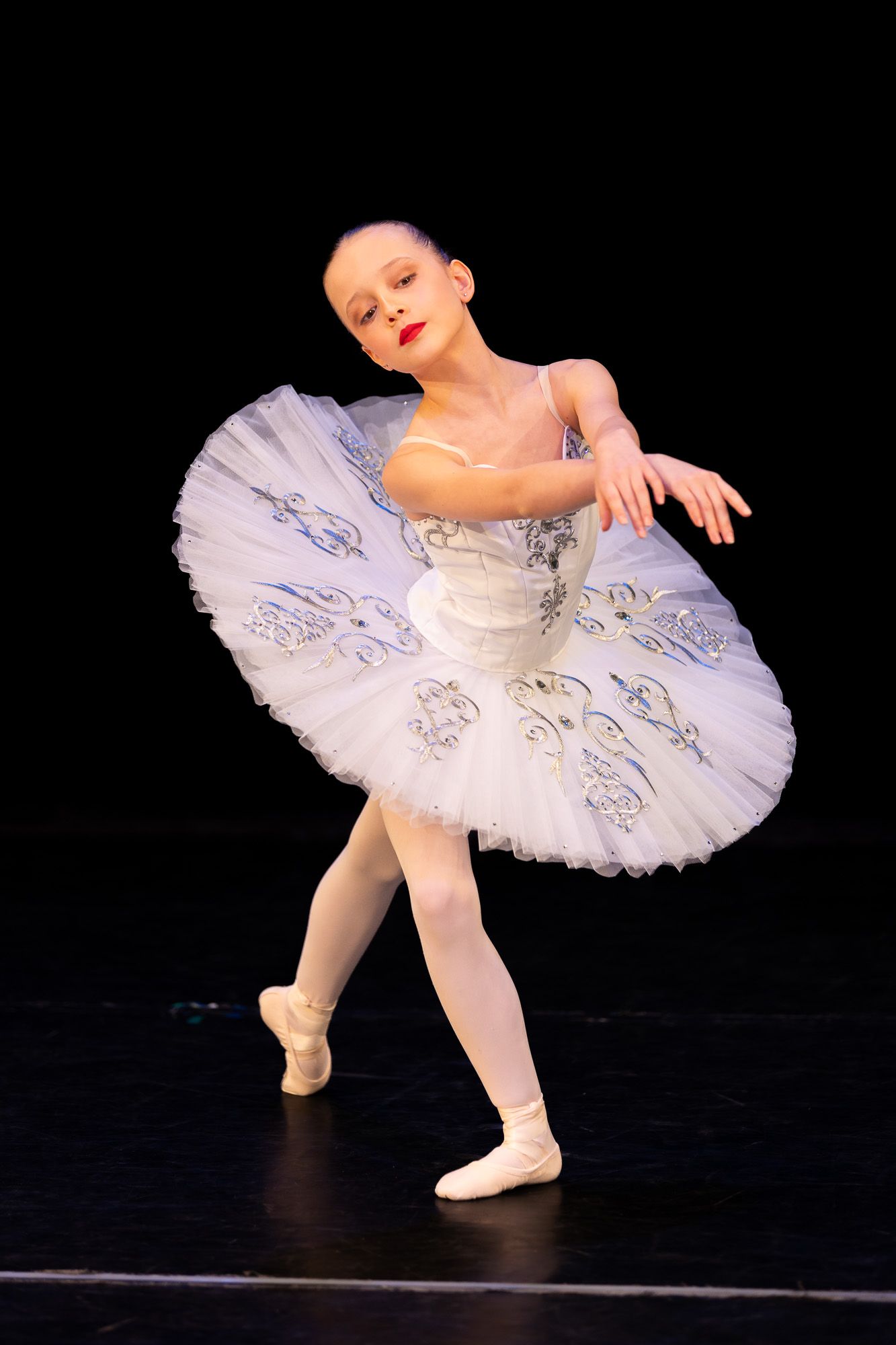 Young ballerina in white tutu performs graceful pose on stage during ballet recital.