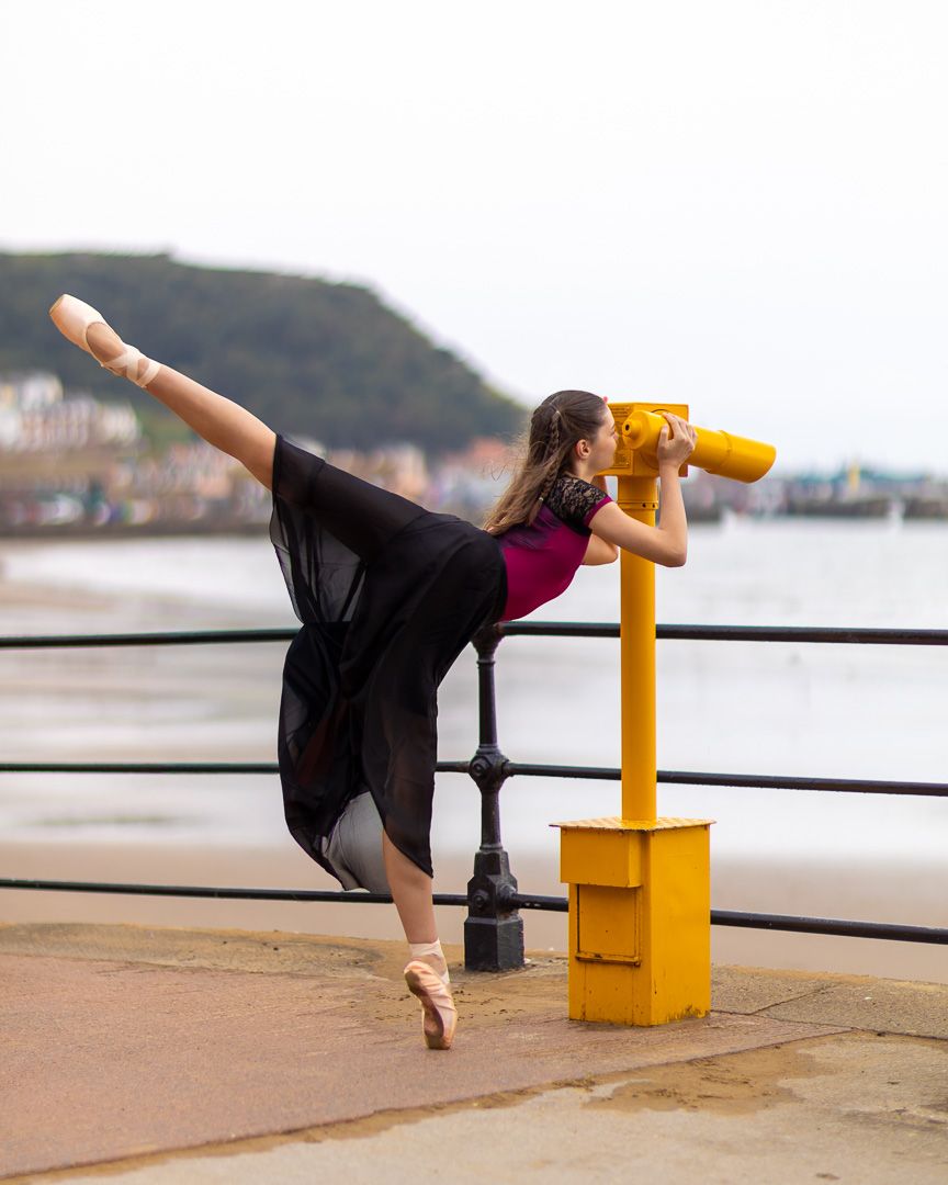Dance poses performed along a seaside railing with beach and cliffs in background.