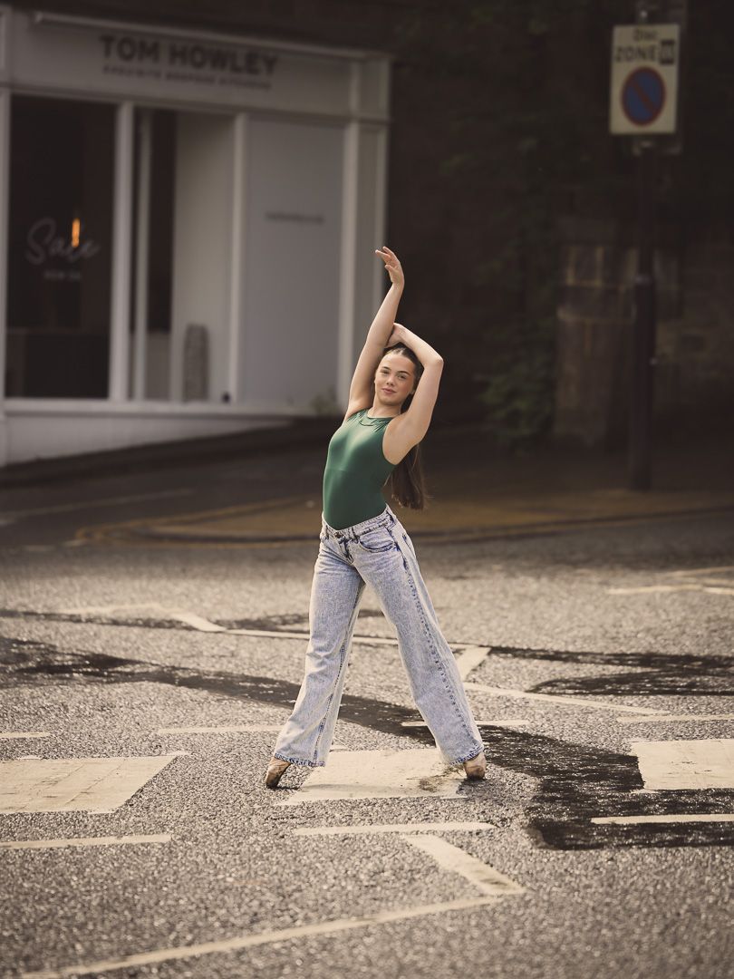 Dancer in casual wear performs an expressive movement on a city street.