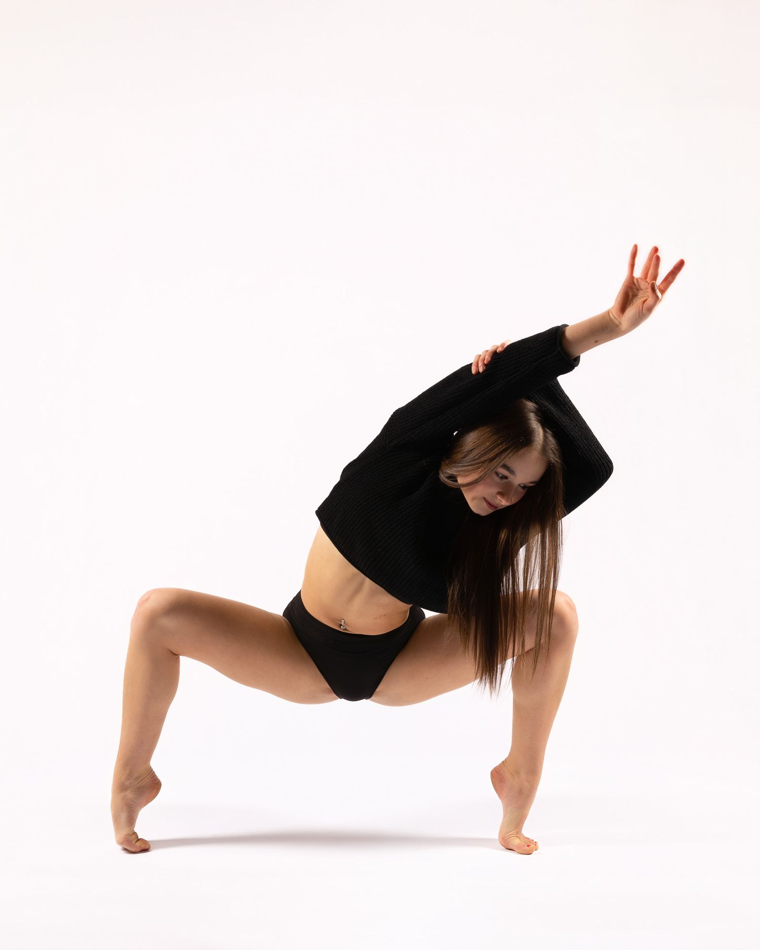Modern dancer in black performs expressive contemporary dance movements against white backdrop.