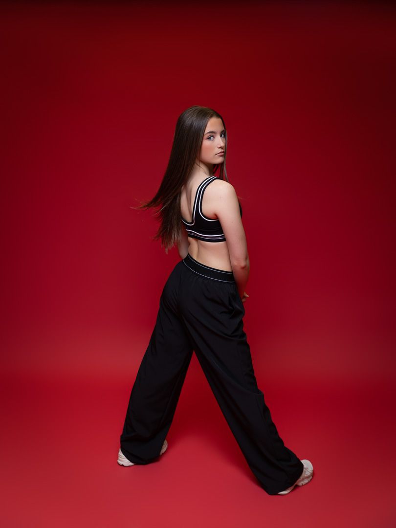 Young woman in black wide-leg pants and crop top poses against a bold red background.