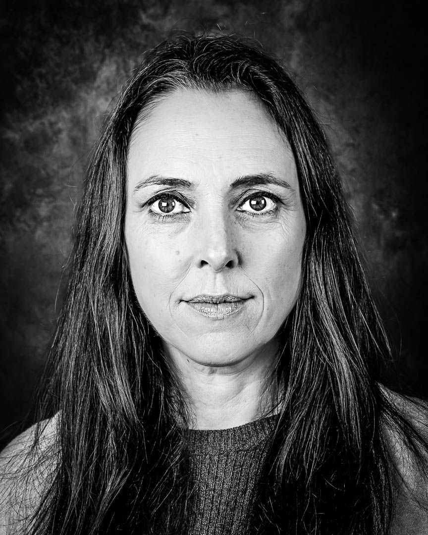 Black and white portrait of a woman with long dark hair against a dark background.