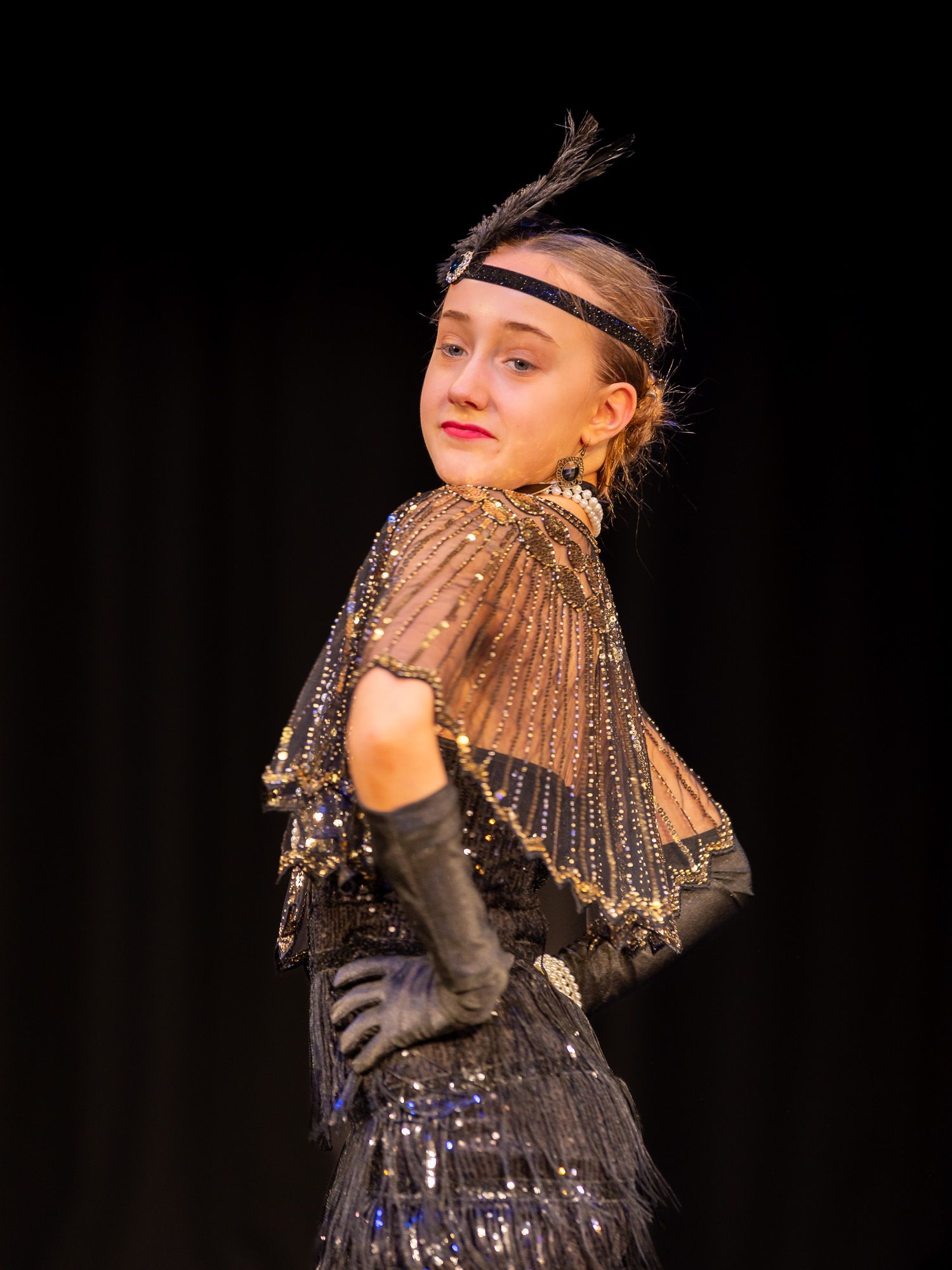 Young performer in 1920s flapper costume with feathered headband and beaded cape on stage.
