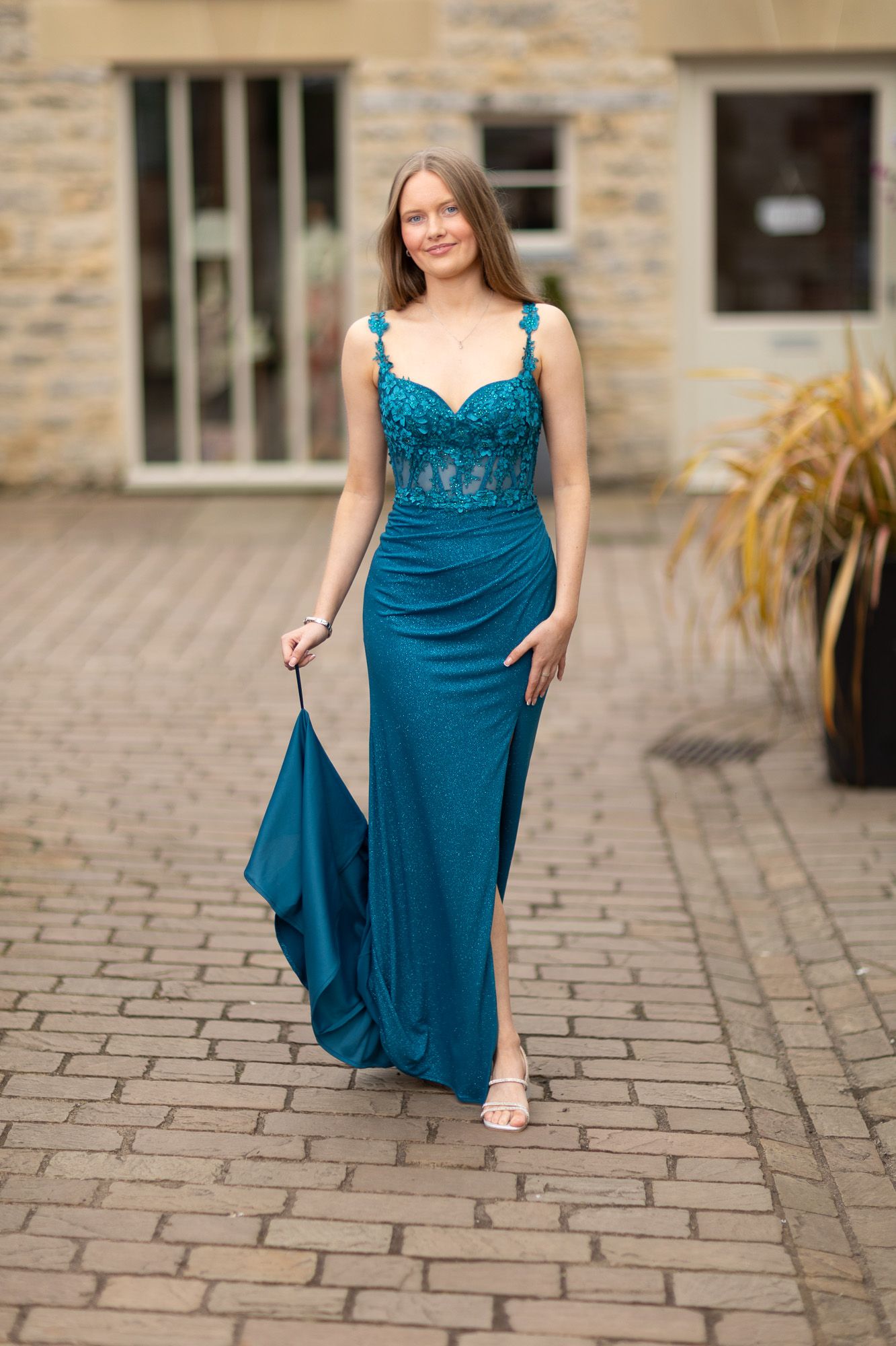 Person in teal formal dress poses on cobblestone courtyard.