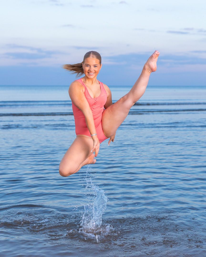 Dancer leaps and splashes in ocean water during sunset photoshoot.