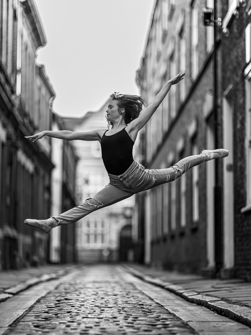 Dancer leaps gracefully across cobblestone street in black attire.