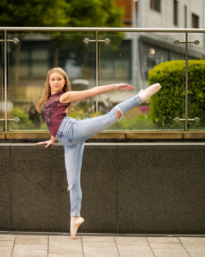 Dancer executing high kicks against an urban backdrop with glass railings.